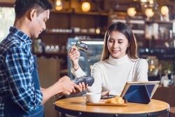 Asian customer woman paying with credit card via contactless nfs technology to Asian Small Coffee shop owner at the female table in cafe, Small business owner and startup in coffee shop concept