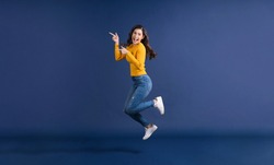 Happy young Asian woman in colorful yellow color casual clothes jumping and presenting to copy space on blue color background, lifestyle and leisure, travel and tourist, travel and vacation concept
