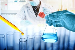 hand of scientist holding flask with dropping yellow liquid to test tube in chemical laboratory background, science laboratory research and development concept