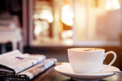Cup of cappuccino with newspaper on the table, coffee shop background, warm tone