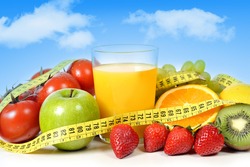 mix of fresh fruit as apple , grapes, strawberries, kiwi and vegetables as tomato with  glass of orange juice all wrapped in measure tape on a blue sky background in healthy nutrition and diet concept