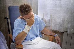 young injured man crying in hospital room sitting alone in pain looking negative and worried for his bad health condition sitting on chair suffering depression on a grunge medical background