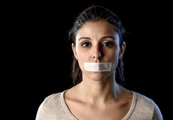close up portrait of young attractive woman with mouth and lips sealed in adhesive tape restrained and abused censored and banned to speak and express opinion in freedom concept