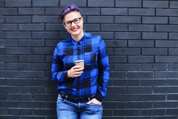 Woman in Blue Flannel Holding Paper Cup Against Black Wall