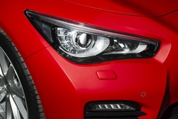 Predatory car headlight and hood of powerful sports car with matte red paint and wheel with silver disc 