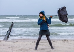 strong wind destroys a woman's umbrella during a beach walk