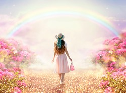 Young lady woman in romantic pink dress, retro hat, bag walking along rose garden path leading to fabulous rainbow unicorn house, flecks of sunlight on road. Tranquil fantasy scene, fairytale hills.
