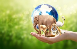 Earth Day or World Animal Day concept. Save planet, protect wildlife nature reserve, protection of endangered species, biological diversity. Elephant, tiger, deer, parrot, flamingo with globe in hand.