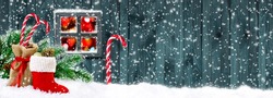 Santa boot and bag with candy cane, gifts and cones on wooden wall background and glowing lights outside the window 