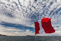 Navigate on the Titicaca Lake, under a blue sky with white clouds, with Peru flag in the close up
