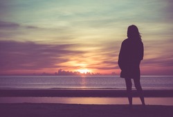Young woman standing on the beach in sea and looking to sunrise.