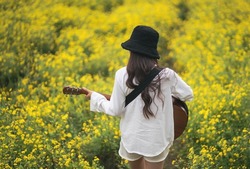 Asian young woman playing guitar and sing music in the park, asian woman palying guitar at yellow flowers garden