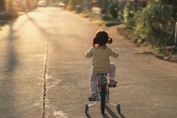 Backside of asian toddler girl child learning to ride bicycle in sunny summer day, kid cycling at park, baby sport concept