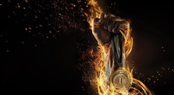 Sport. Man's hand holding up trophy medal. Winner in a competition. Fire and energy