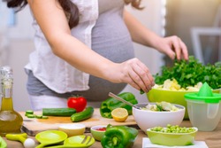 Happy pregnant woman cooking at home, doing fresh green salad, eating many different vegetables during pregnancy, healthy pregnancy concept
