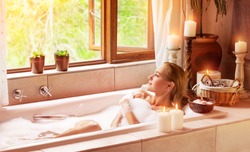 Woman bathing with pleasure, lying down in the tub with foam and looking in the window, spending time in luxury spa resort