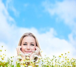 Happy young female lying on the flower field, over blue cloudy sky, with copyspace, leisure, fun and wellness concept