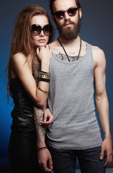 fashionable beautiful lovely couple in sunglasses. bearded Hipster boy and beauty girl with tattoo over blue background