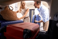 Caucasian marriage couple packing luggage into car trunk for holiday