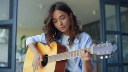 Pretty girl practicing music on guitar. Female guitarist playing chords on acoustic guitar in living room. Happy woman showing yes gesture with hand. Positive lady enjoying success at home
