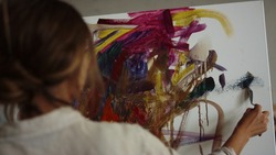Talented female artist creating picture with palette knife in modern studio. Creative woman using easel and canvas for work in art studio. Inspired painter drawing colorful artwork indoors.