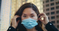 Portrait of pretty asian girl wearing face mask looking camera on city street. Healthy calm woman care of safety during pandemic period in big town closeup. Responsible behavior in people life.