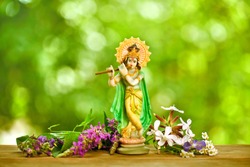 Hindu god Krishna. Statue with fresh flowers on a green bokeh background.