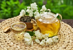 Jasmine green tea in a glass teapot with a glass cup and fresh blossoms