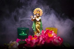 Hindu god Krishna. Statue with a smoke and lotus flowers on a black background