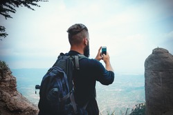 man hiker taking photo with smart-phone at mountain peak cliff