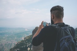 Young hipster taking picture with phone camera of landscape