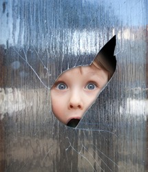 boy looks through a broken window