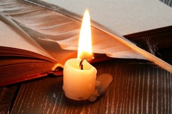 Art concept. One lighting candle near open notebook and quill pen
