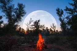 camp fire on forest glade with huge moon rising above, twilight outdoor camping scene