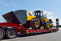 Big tractor machine heavy tool on truck transportation motion speed on road under blue sky