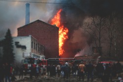 Massive large blaze fire in the city, brick factory building on fire, hell major fire explosion flame blast,  with firefighters team firemen on duty, arson, burning house damage destruction 