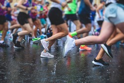 Marathon runners competition in the rain close-up, view of footwear running shoes during half-marathon on the city asphalt streets with water splash, crowd of joggers in motion, outdoor training