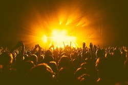 A crowded concert hall with scene stage orange and yellow lights, rock show performance, with people silhouette, colourful confetti explosion fired on dance floor air during a concert festival
