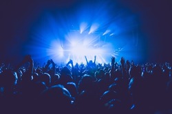 A crowded concert hall with scene stage lights in blue tones, rock show performance, with people silhouette, on a dance floor air during a concert festival