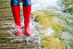 red rubber boots in water on a wooden bridge, the river overflowed its banks.