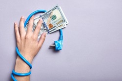 Conceptual image about the high economic cost of electric power and the increase in energy rates: power cable wrapped around one arm, the hand holds dollar banknotes.