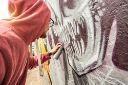 Street artist painting colorful graffiti on public wall - Modern art concept with urban guy performing and preparing live murales with multi color aerosol spray - Sunshine filter with focus on monster