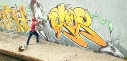 Wide view of street artist painting colorful graffiti on generic wall - Modern art concept with urban guy performing and preparing live murale with multi color aerosol spray - Retro vintage filter