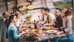 Young people dining and having fun drinking red wine together on balcony rooftop dinner party - Happy friends eating bbq food at restaurant patio - Millennial life style concept on warm evening filter