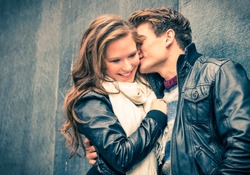 Young happy couple of lovers at beginning of love story - Handsome man whispers soft kisses in beautiful woman ear - Fall fashion concept with boyfriend and girlfriend on a cold vintage filtered look
