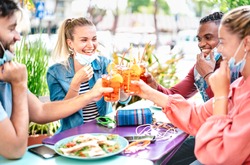 Friends drinking spritz at cocktail bar with open face mask - New normal friendship concept with happy people having fun together toasting drinks at restaurant - Bright filter with focus on left woman