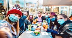 Friends taking selfie outside at cocktail bar - New normal lifestyle concept with young people having fun together at restaurant cafe covered by face masks - Vivid filter with focus on central guy 