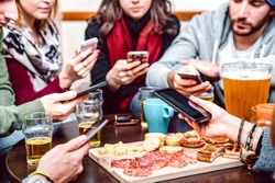 Side angle view of hands with cellphones at beer bar restaurant - People sharing time together with mobile smartphones at pre dinner event - Lifestyle concept on vivid filter with focus on right phone