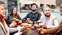 Young friends drinking beer wearing face mask - New normal lifestyle concept with people having fun together talking on happy hour at hipster brewery bar - Bright warm filter with focus on central guy