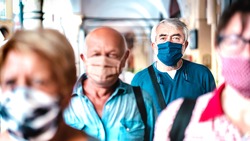 Urban crowd of adult citizens walking on city street during pandemic - New reality life style concept with senior people with covered faces - Selective focus on man with blue protective mask